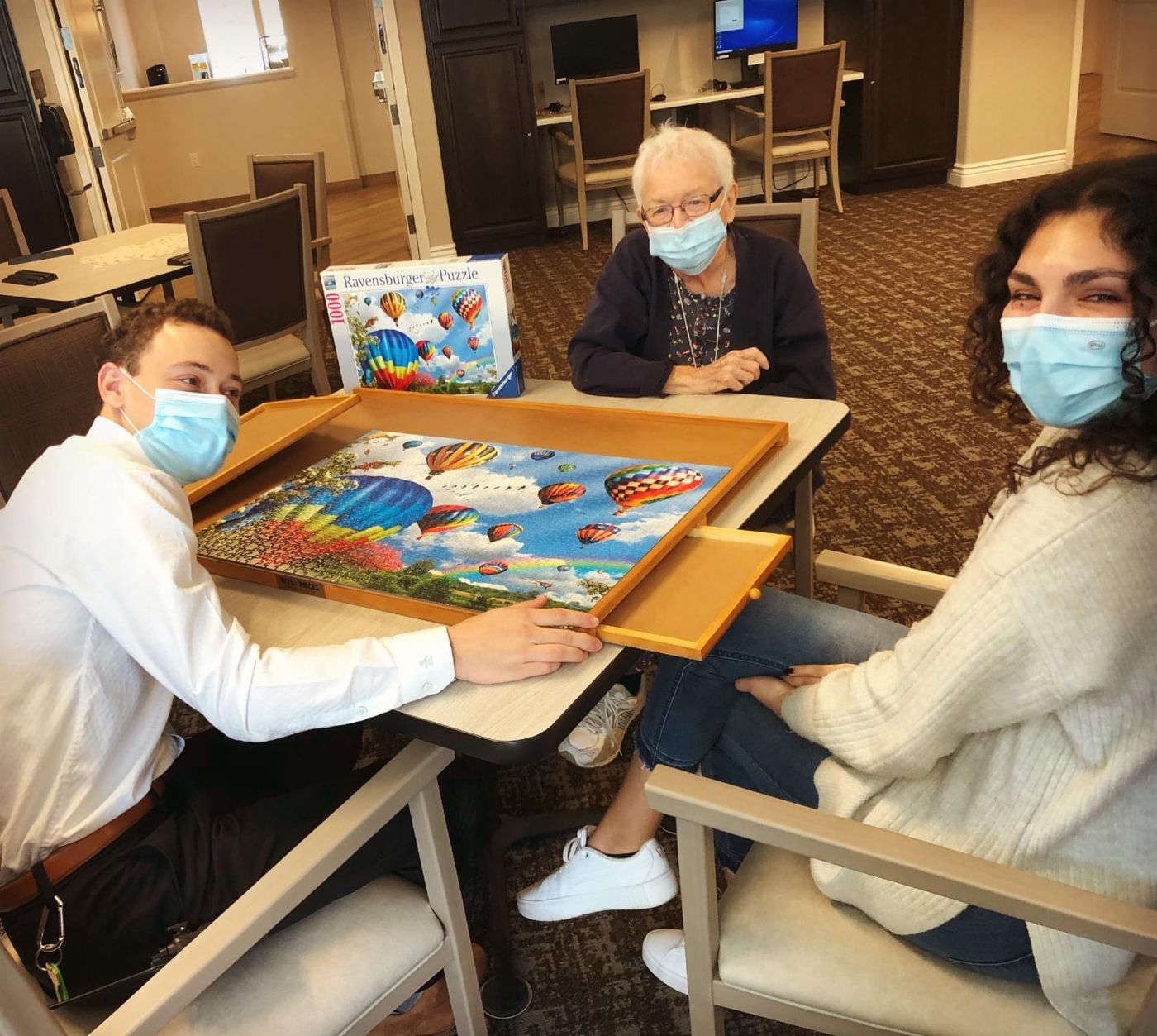 Tristan and Ileana at a table with a resident at Oakmont of Novato, working on a puzzle